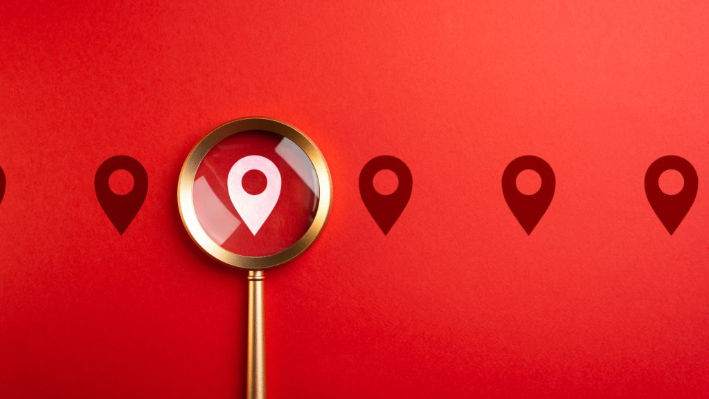 Roter Hintergrund und eine Lupe die auf das Standort Zeichen zeigt