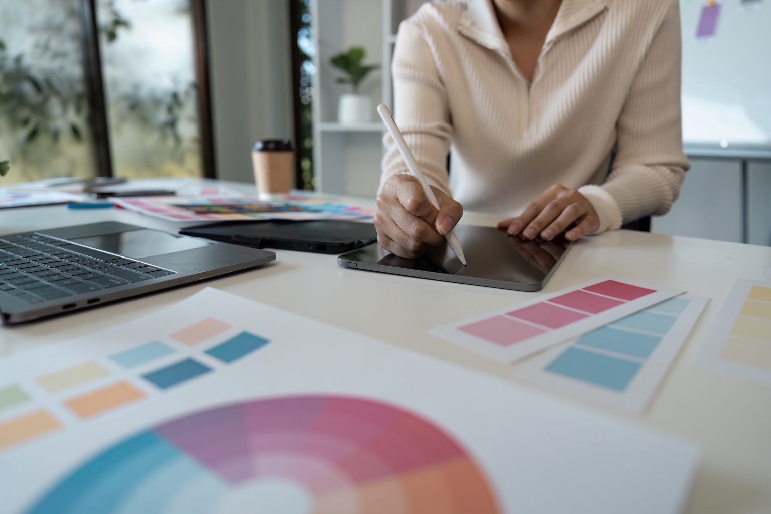 Frau sitzt am Schreibtisch mit Ipad und verschiedenen Farbpaletten um sich herum