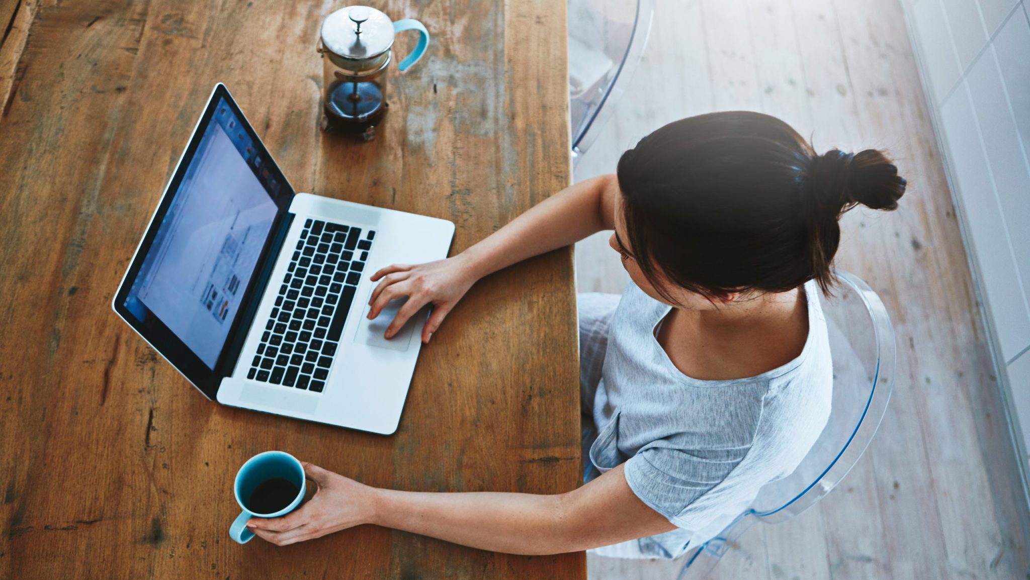 Frau sitzt an Tisch mit geöffnete Laptop und Kaffee