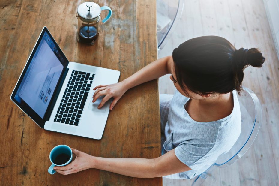 Frau sitzt an Tisch mit geöffnete Laptop und Kaffee